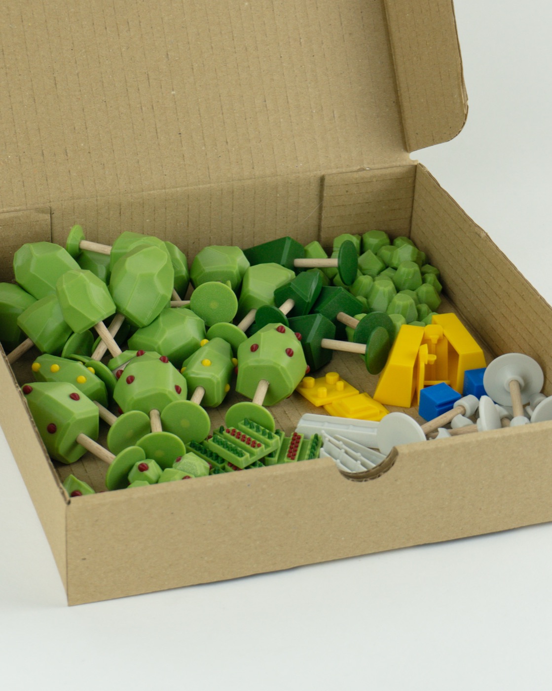 La boîte du kit ouverte, remplie d'arbres, de buissons, de pièces jaunes et bleues et de socles.