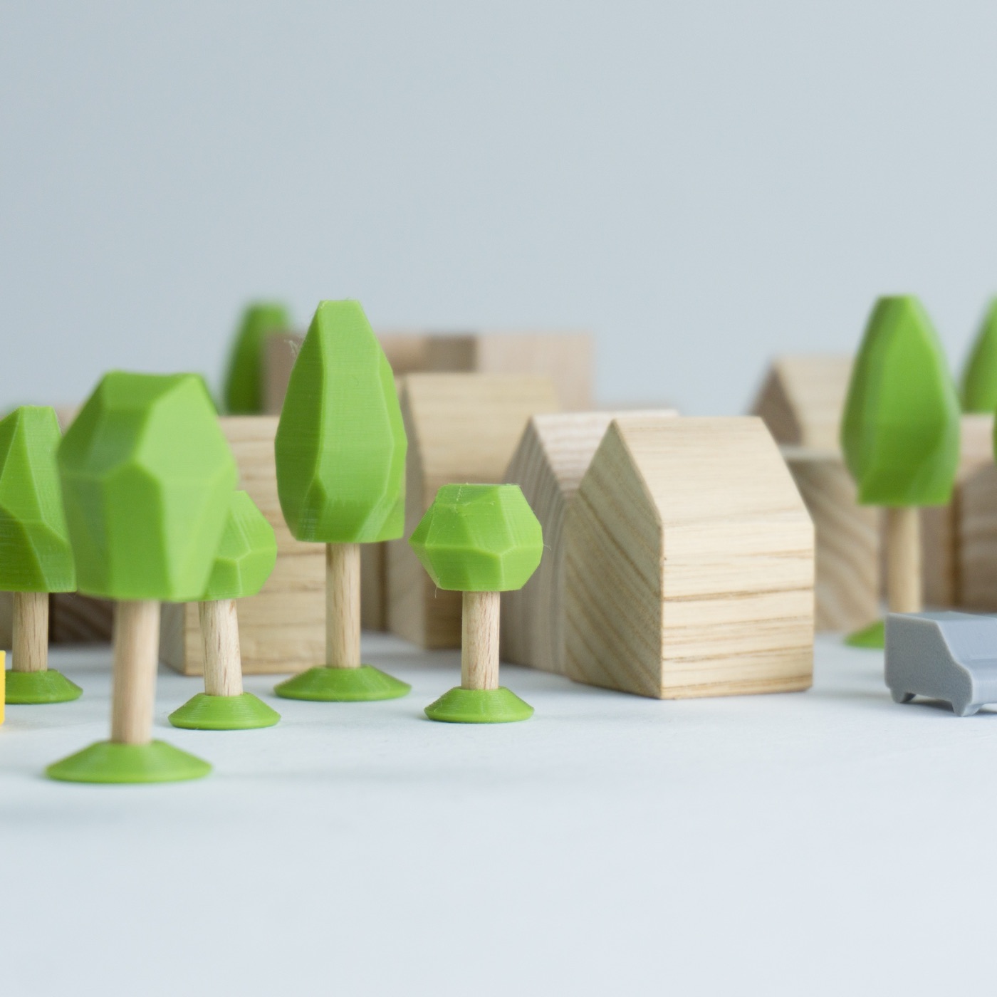 Gros plan sur trois arbres du kit : feuillage vert imprimé, baguette de bois, socle conique, devant une maison en bois clair.