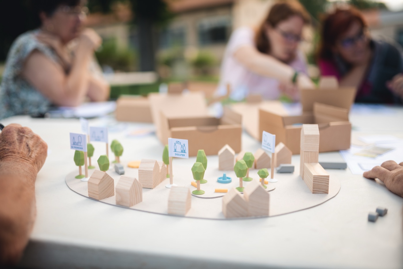 Autour d'une table, plusieurs participants composent ensemble une maquette de bourg, les boîtes du kit ouvertes à portée de main.